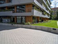 an open paved area with concrete walling, grass and a patio on one side