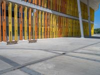 a concrete structure made into rows of orange and yellow poles are on a cement sidewalk