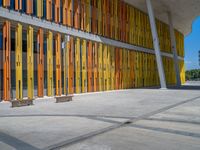 a concrete structure made into rows of orange and yellow poles are on a cement sidewalk