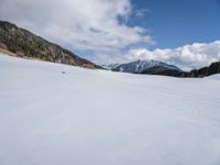 a person on skis traveling along a snowy field near a lodge area and mountains