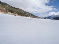 a person on skis traveling along a snowy field near a lodge area and mountains