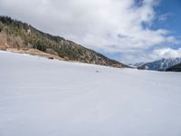 a person on skis traveling along a snowy field near a lodge area and mountains