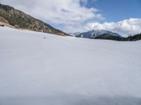 a person on skis traveling along a snowy field near a lodge area and mountains