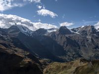 a lone person stands in the mountains, staring out at snow on top of the peaks