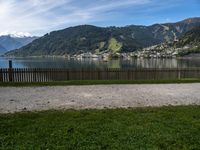 a man with a bike leaning against a fence in front of the water, in front of mountains