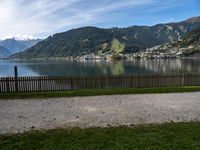 a man with a bike leaning against a fence in front of the water, in front of mountains