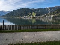 a man with a bike leaning against a fence in front of the water, in front of mountains