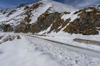 man snow skis near a wall and a car in the road with rocky mountains