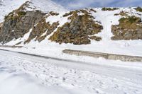 man snow skis near a wall and a car in the road with rocky mountains