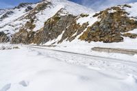 man snow skis near a wall and a car in the road with rocky mountains