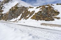 man snow skis near a wall and a car in the road with rocky mountains