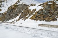 man snow skis near a wall and a car in the road with rocky mountains