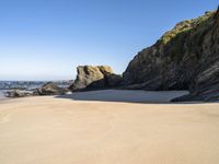 a sandy beach near the ocean and cliffs with water nearby on a clear day with no one in sight