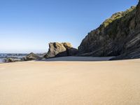 a sandy beach near the ocean and cliffs with water nearby on a clear day with no one in sight