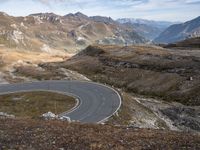 a paved curved road surrounded by mountains in the distances area of mountainous countryside, looking towards a valley