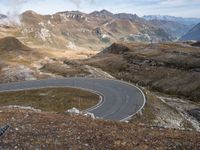 a paved curved road surrounded by mountains in the distances area of mountainous countryside, looking towards a valley