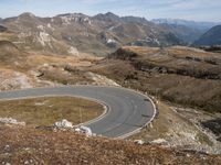 a paved curved road surrounded by mountains in the distances area of mountainous countryside, looking towards a valley