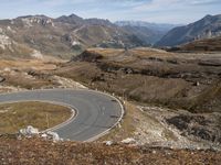 a paved curved road surrounded by mountains in the distances area of mountainous countryside, looking towards a valley