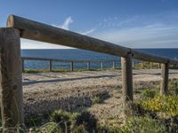 a wooden fence next to a sea and some grass on the ground near a beach