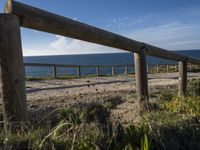 a wooden fence next to a sea and some grass on the ground near a beach