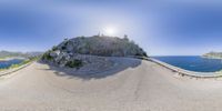 an artistic fisheye lens image of a winding road next to the ocean with sun shining