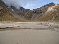 a motorcycle is parked on a beach near the mountains and some water with clouds hovering above