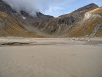 a motorcycle is parked on a beach near the mountains and some water with clouds hovering above