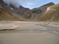 a motorcycle is parked on a beach near the mountains and some water with clouds hovering above