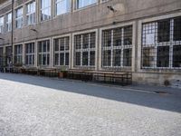 a street in an old part of europe with benches and tables by the windows with plants growing out