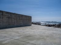 the beach with some rocks and rocks in front of a concrete wall that has a sea behind it
