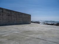 the beach with some rocks and rocks in front of a concrete wall that has a sea behind it