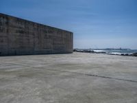 the beach with some rocks and rocks in front of a concrete wall that has a sea behind it