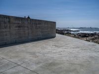 the beach with some rocks and rocks in front of a concrete wall that has a sea behind it