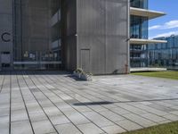 an outdoor square patio in front of a building with large windows and a planter next to it