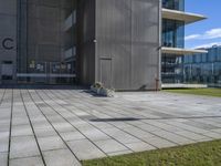 an outdoor square patio in front of a building with large windows and a planter next to it