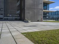 an outdoor square patio in front of a building with large windows and a planter next to it