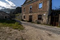 an old house with the street visible to the left side with grass and rocks everywhere on the ground