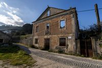 an old house with the street visible to the left side with grass and rocks everywhere on the ground