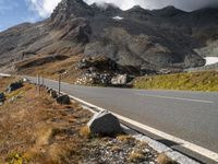 an empty mountain highway with a vehicle in the middle of it and snow capped mountains in the distance