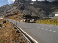 an empty mountain highway with a vehicle in the middle of it and snow capped mountains in the distance