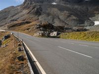 an empty mountain highway with a vehicle in the middle of it and snow capped mountains in the distance