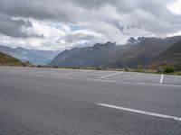 a motorcycle parked in an empty parking lot between mountains in the mountains on a cloudy day