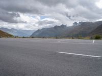 a motorcycle parked in an empty parking lot between mountains in the mountains on a cloudy day