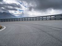 a curved road in the middle of nowhere with mountains in the background and overcast sky