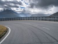 a curved road in the middle of nowhere with mountains in the background and overcast sky