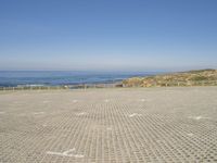 view of ocean and a beach from a bench at a park with sand and brick walkways