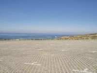 view of ocean and a beach from a bench at a park with sand and brick walkways