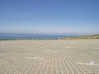 view of ocean and a beach from a bench at a park with sand and brick walkways