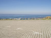 view of ocean and a beach from a bench at a park with sand and brick walkways