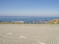 view of ocean and a beach from a bench at a park with sand and brick walkways